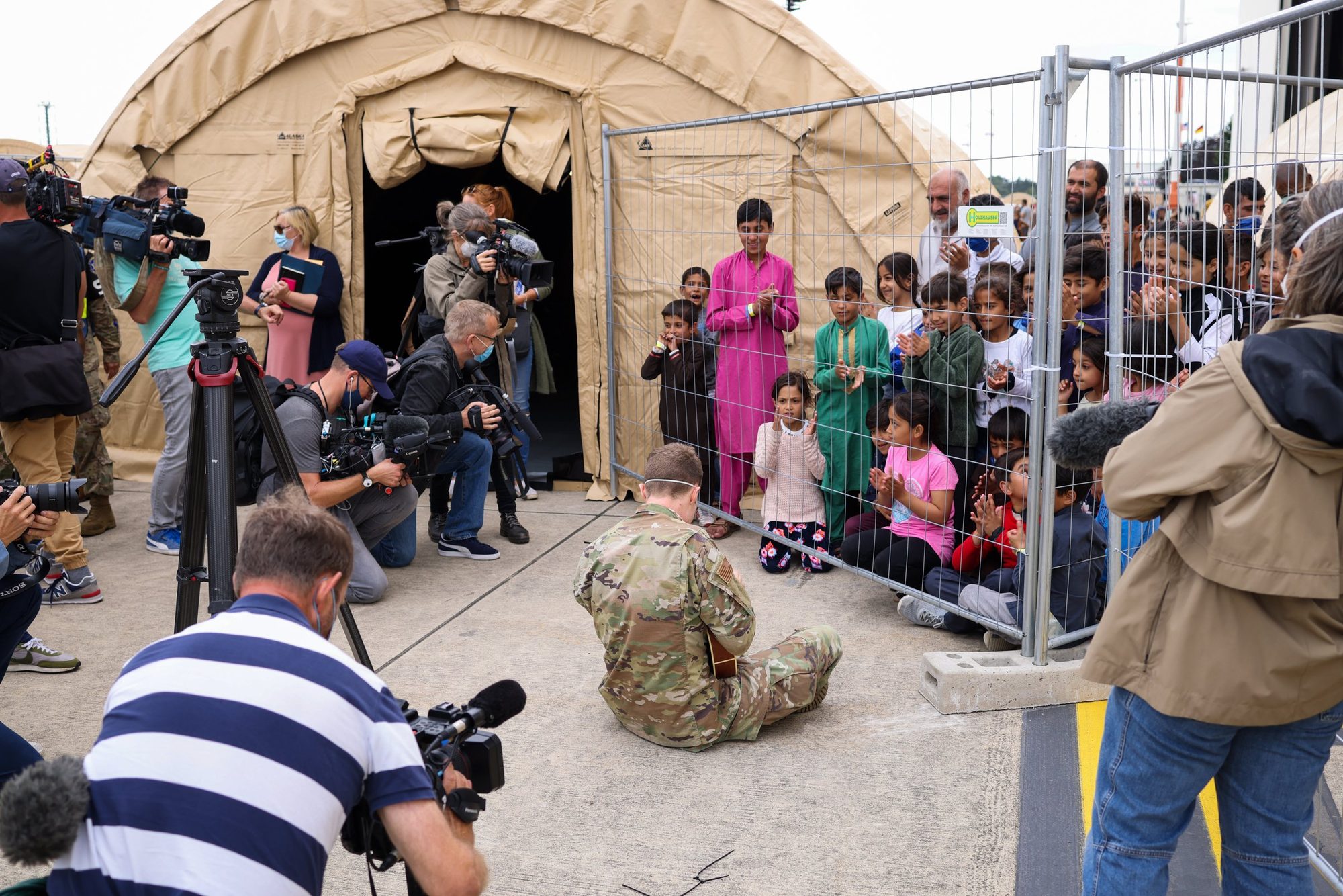 Media photographers document a US soldier entertaining Afghan evacuee children at Ramstein Air Base, 2021