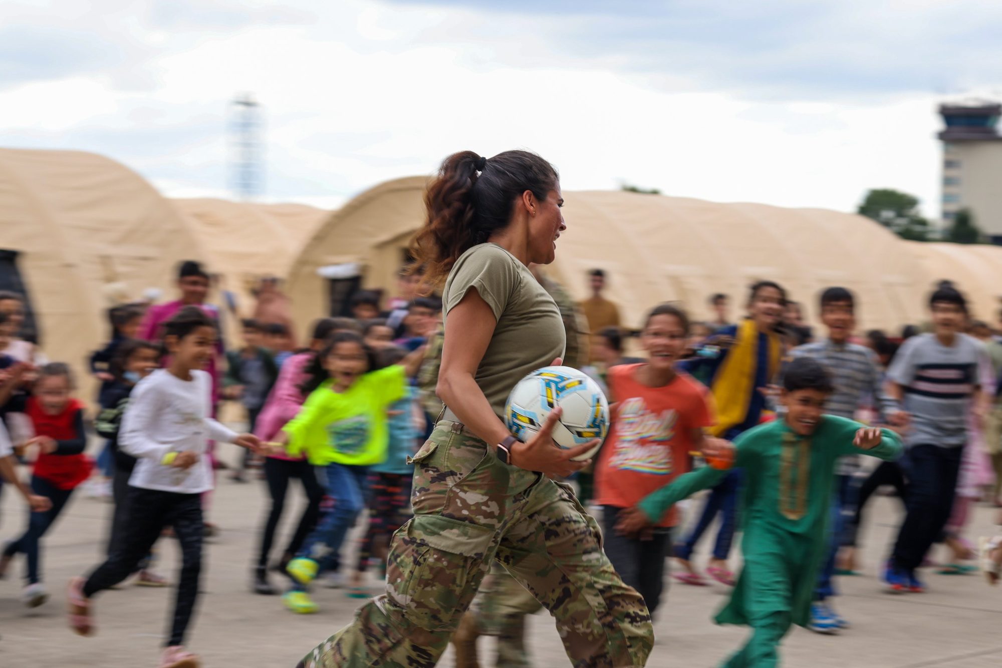 A US soldier plays football with Afghan evacuee children at Ramstein Air Base, 2021